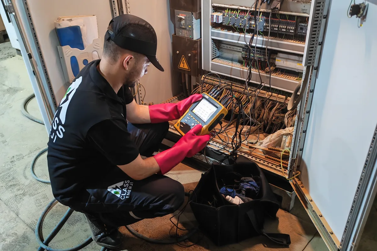 A Class Enerji mühendisi elektrik panosunda yalıtımlı eldivenlerle güç analizörü ölçümü yapıyor